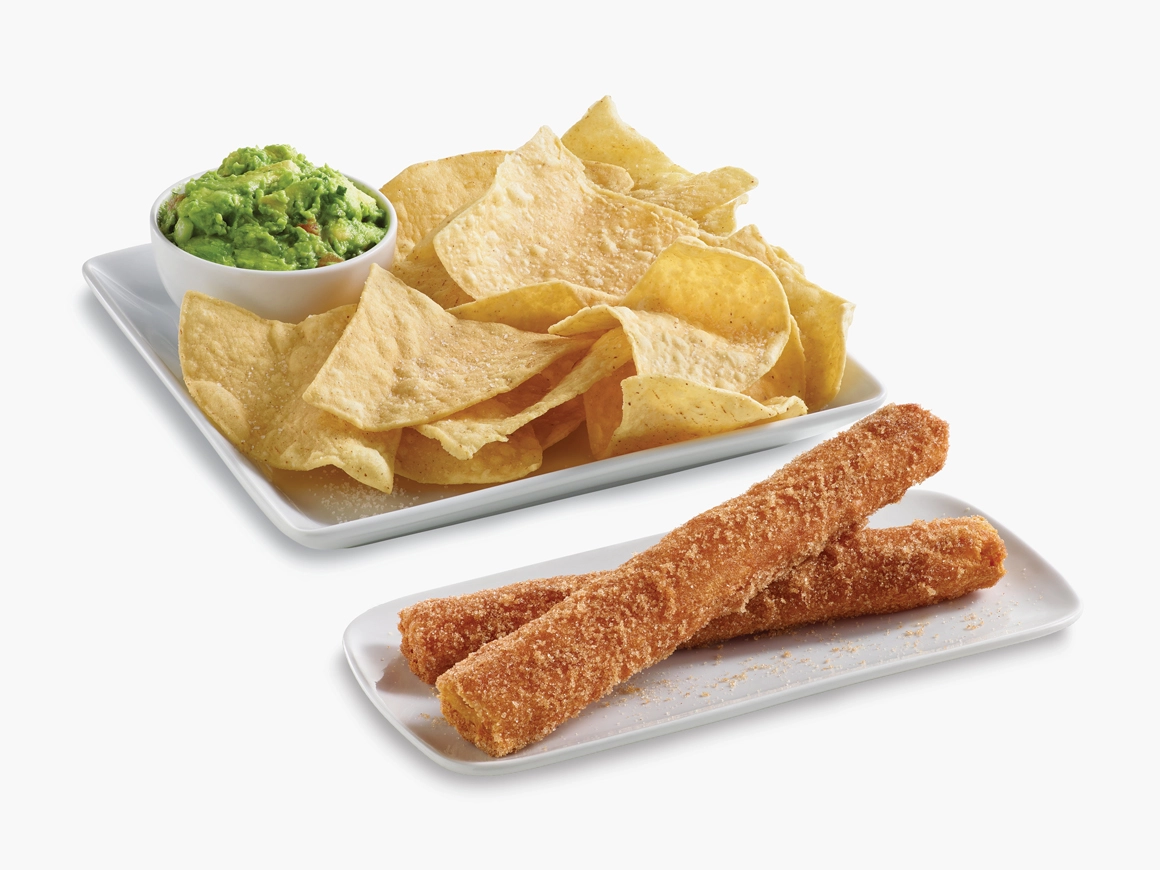 Chips on a plate with a cup of guacamole and two churros on a plate